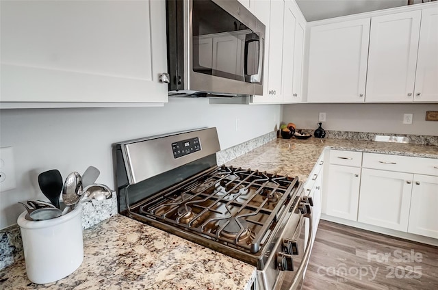 kitchen featuring light stone counters, light hardwood / wood-style floors, white cabinets, and appliances with stainless steel finishes