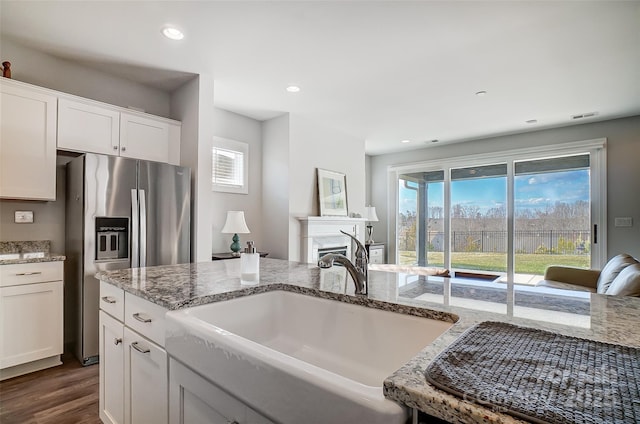 kitchen featuring white cabinetry, sink, stainless steel fridge with ice dispenser, light stone countertops, and dark wood-type flooring