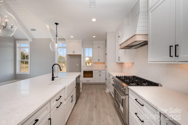 kitchen featuring premium range hood, light stone counters, high end range, hanging light fixtures, and white cabinets