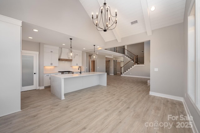 kitchen with white cabinetry, a spacious island, custom exhaust hood, hanging light fixtures, and light hardwood / wood-style flooring