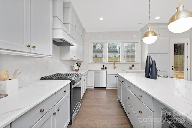 kitchen featuring pendant lighting, premium range hood, stainless steel appliances, light stone counters, and tasteful backsplash