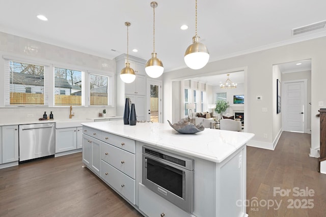 kitchen featuring hanging light fixtures, dark hardwood / wood-style floors, a kitchen island, stainless steel appliances, and light stone countertops