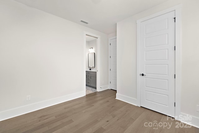 unfurnished bedroom with ensuite bathroom and hardwood / wood-style floors