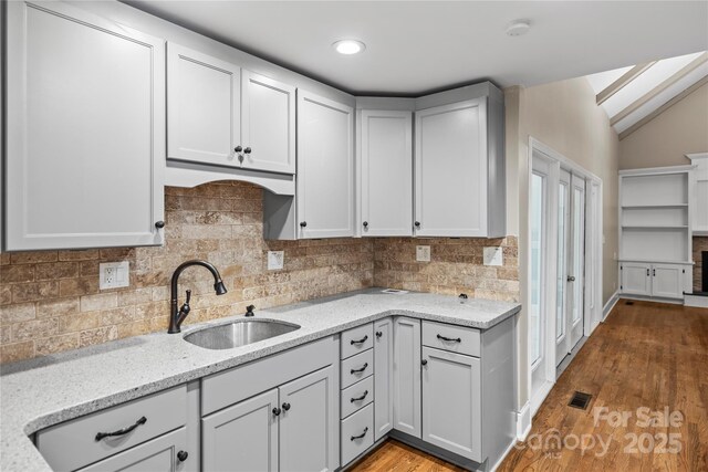 kitchen with lofted ceiling, sink, backsplash, light stone counters, and light wood-type flooring