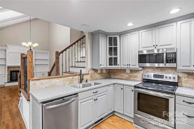 kitchen featuring sink, hanging light fixtures, stainless steel appliances, light stone countertops, and light hardwood / wood-style floors