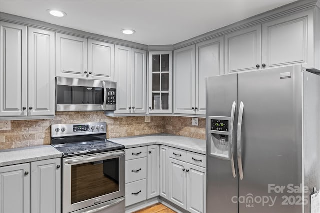 kitchen featuring tasteful backsplash, stainless steel appliances, light stone countertops, and gray cabinetry