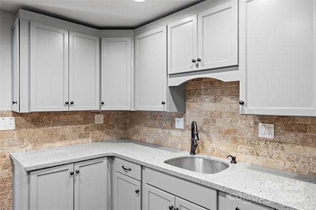 kitchen with light stone counters, sink, and backsplash