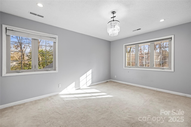 carpeted spare room featuring a chandelier and a textured ceiling