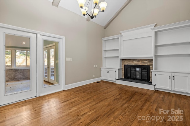 unfurnished living room with dark hardwood / wood-style floors, a stone fireplace, high vaulted ceiling, and a notable chandelier