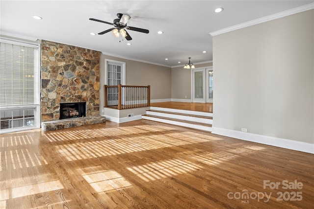 unfurnished living room featuring crown molding, a stone fireplace, light hardwood / wood-style flooring, and ceiling fan with notable chandelier