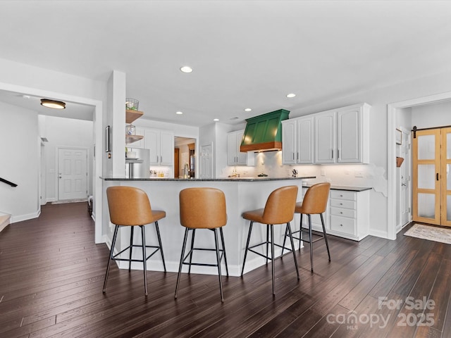 kitchen with stainless steel refrigerator, dark hardwood / wood-style flooring, kitchen peninsula, and white cabinets