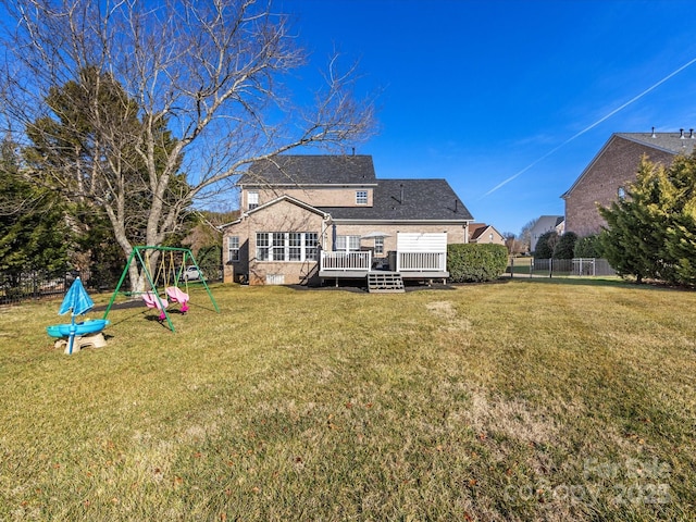 rear view of house with a wooden deck, a lawn, and a playground