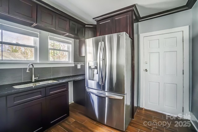 kitchen with stainless steel refrigerator with ice dispenser, sink, dark brown cabinetry, and dark stone counters