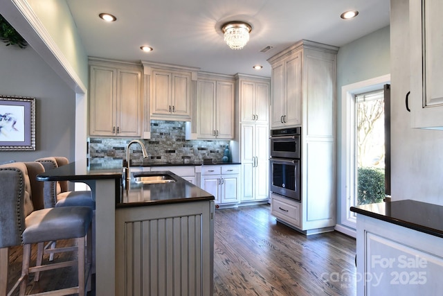 kitchen featuring double oven, sink, backsplash, a kitchen bar, and dark wood-type flooring