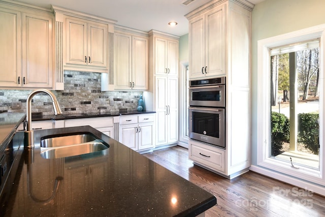 kitchen featuring cream cabinets, sink, double oven, and backsplash