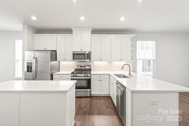 kitchen featuring appliances with stainless steel finishes, sink, backsplash, white cabinetry, and a center island