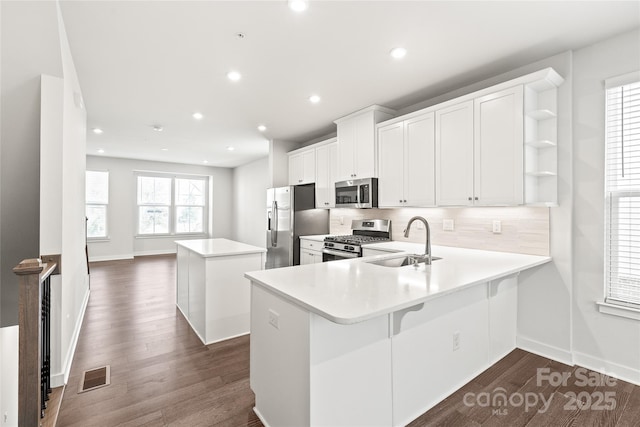 kitchen with kitchen peninsula, appliances with stainless steel finishes, sink, backsplash, and white cabinetry