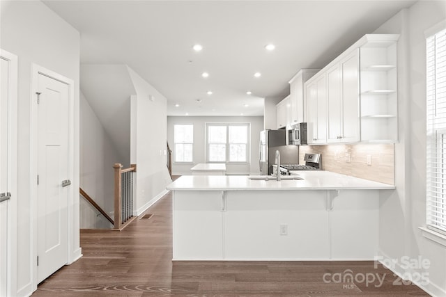 kitchen featuring white cabinetry, stainless steel appliances, decorative backsplash, a kitchen breakfast bar, and kitchen peninsula