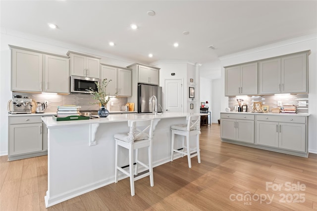 kitchen with an island with sink, appliances with stainless steel finishes, a kitchen breakfast bar, light countertops, and gray cabinetry