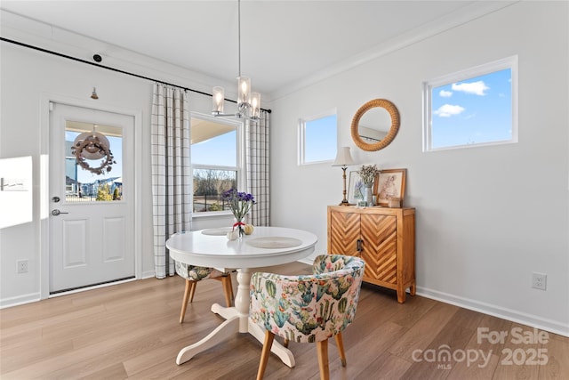 dining area featuring light wood-type flooring, crown molding, baseboards, and a notable chandelier