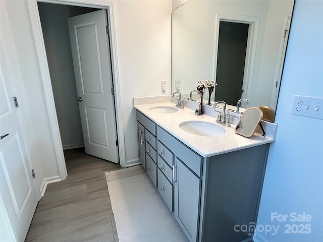 full bath featuring double vanity, baseboards, a sink, and wood finished floors