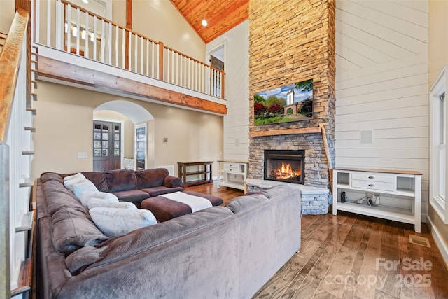 living room featuring hardwood / wood-style flooring, a towering ceiling, a stone fireplace, and wooden ceiling