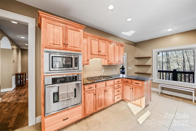 kitchen featuring stainless steel appliances, dark stone countertops, light tile patterned floors, and light brown cabinetry