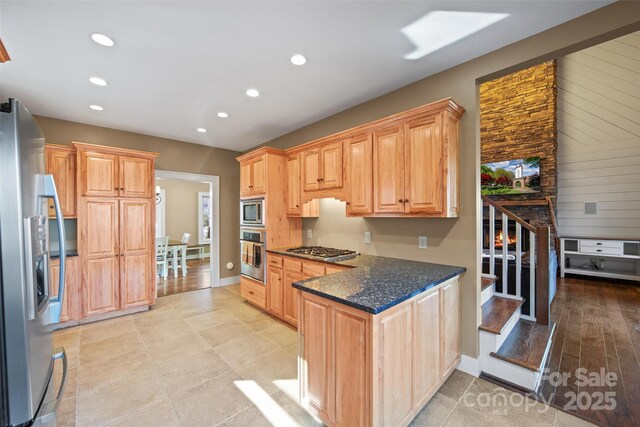 kitchen featuring light brown cabinetry, stainless steel appliances, and dark stone counters