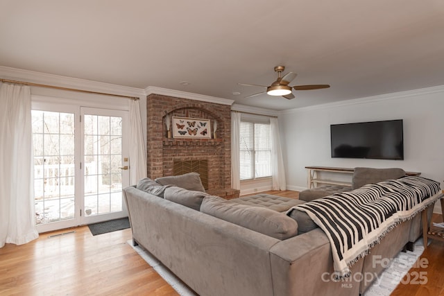 living room with a brick fireplace, light hardwood / wood-style flooring, ornamental molding, and ceiling fan