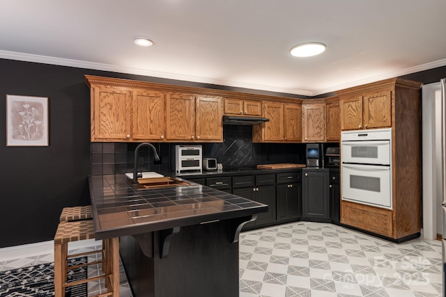 kitchen featuring sink, white double oven, a breakfast bar, ornamental molding, and kitchen peninsula