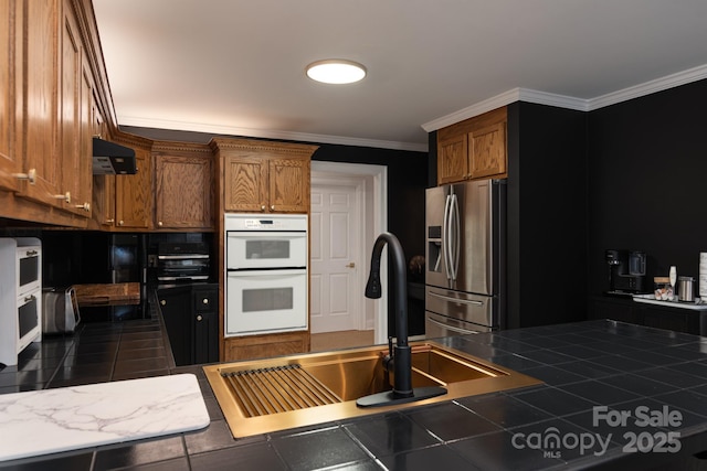 kitchen featuring sink, double oven, tile counters, ornamental molding, and stainless steel fridge with ice dispenser