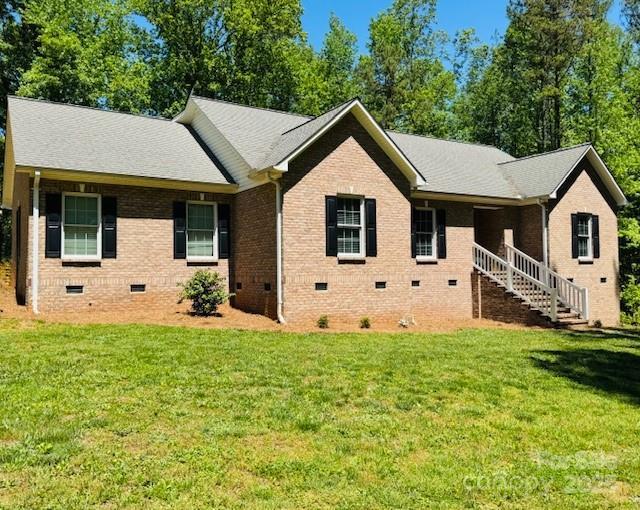 ranch-style home with brick siding, a front lawn, roof with shingles, and crawl space
