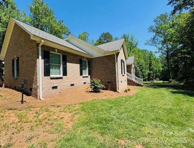 view of side of home with brick siding, a yard, and crawl space