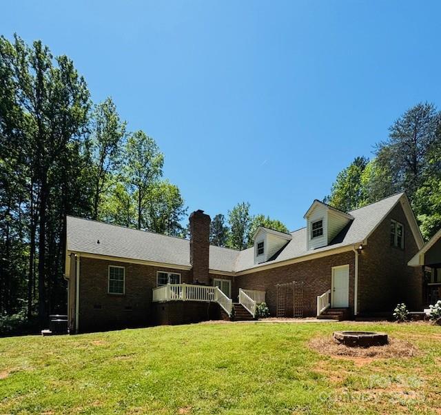 rear view of property featuring brick siding, a wooden deck, entry steps, a chimney, and a lawn