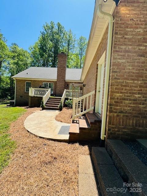 rear view of property with brick siding, a wooden deck, and a chimney