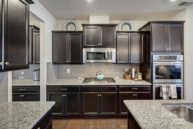 kitchen with appliances with stainless steel finishes, tasteful backsplash, dark brown cabinetry, and dark hardwood / wood-style flooring