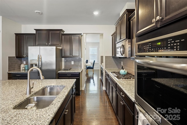 kitchen featuring sink, backsplash, light stone countertops, stainless steel appliances, and dark brown cabinetry