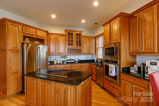 kitchen featuring appliances with stainless steel finishes, a center island, light wood-type flooring, and dark stone counters