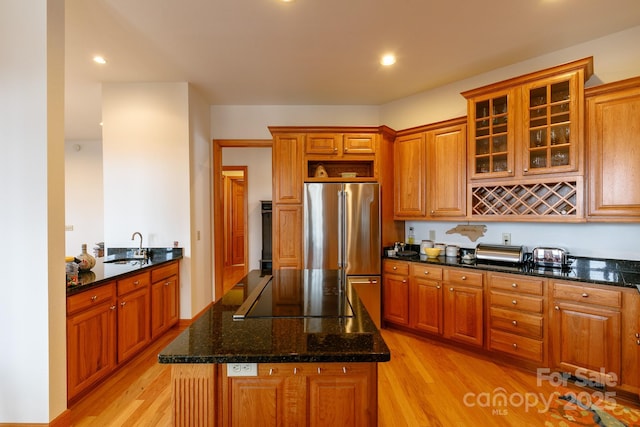 kitchen featuring sink, high end refrigerator, light wood-type flooring, and dark stone counters