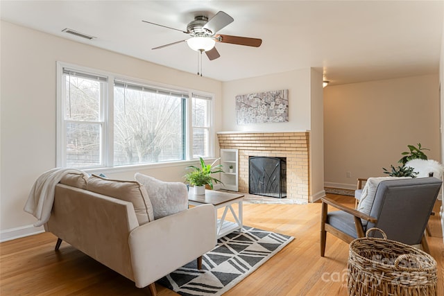 living room with ceiling fan, wood-type flooring, and a brick fireplace