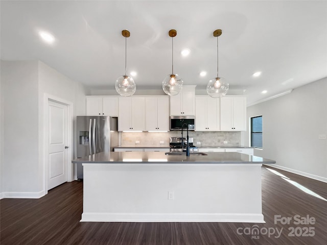 kitchen featuring white cabinetry, stainless steel appliances, decorative light fixtures, and a kitchen island with sink