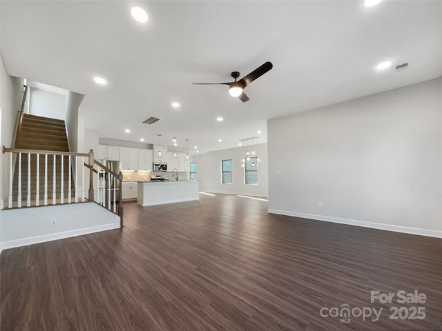 unfurnished living room with sink, ceiling fan with notable chandelier, and dark wood-type flooring