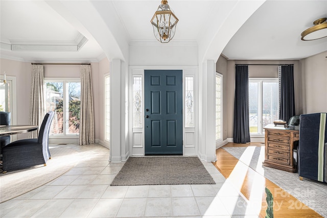 foyer entrance featuring light tile patterned floors, crown molding, and a notable chandelier