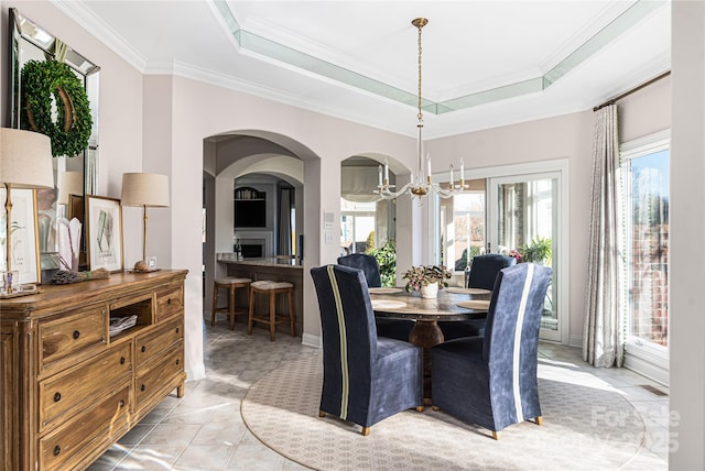 tiled dining area with a tray ceiling, ornamental molding, and a chandelier