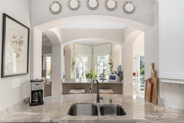 interior space with white cabinetry, sink, a wealth of natural light, and light stone countertops