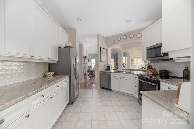 kitchen featuring sink, stainless steel appliances, light stone countertops, decorative backsplash, and white cabinets