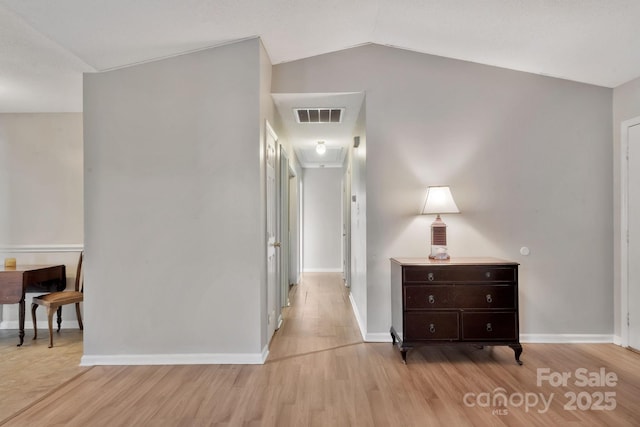 hallway featuring lofted ceiling, light wood finished floors, baseboards, and visible vents