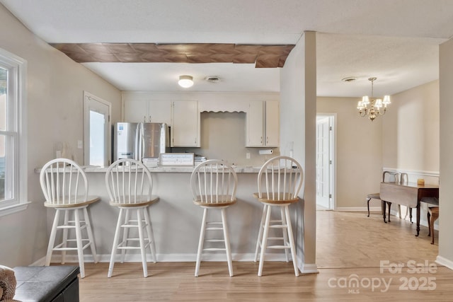 kitchen with baseboards, stainless steel fridge with ice dispenser, a peninsula, white cabinetry, and pendant lighting