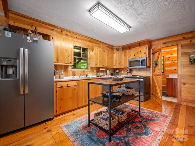 kitchen with sink, appliances with stainless steel finishes, wood walls, and light wood-type flooring