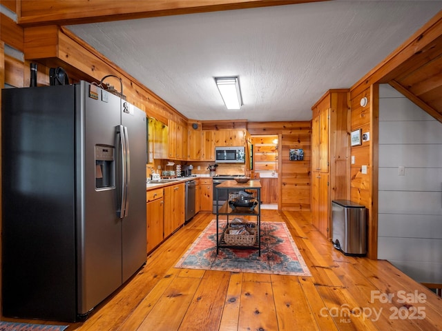 kitchen featuring light hardwood / wood-style floors, wood walls, and appliances with stainless steel finishes